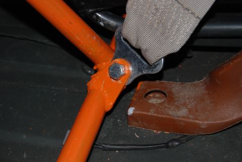 1982 Ford Bronco - Close-up of a seatbelt mounting bracket attached to an orange roll cage tube inside a vehicle.