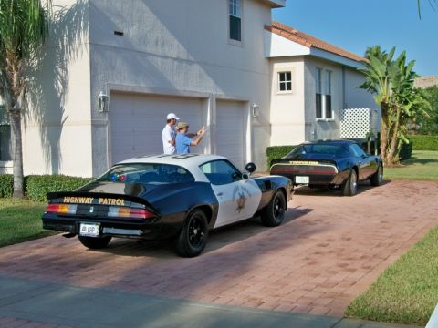 1977 Pontiac Trans Am - A 1977 Pontiac Trans Am police car is parked in a driveway next to another Trans Am, with two people standing nearby.