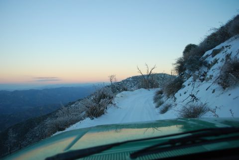 1996 Ford Bronco - View from inside a green vehicle driving on a snow-covered mountain road as the sun rises.
