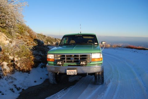 1996 Ford Bronco - A green 1996 Ford Bronco is parked on a snowy road with a clear blue sky above.