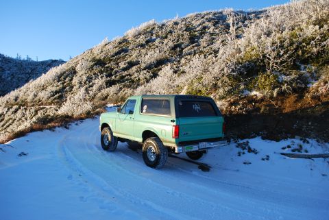 1996 Ford Bronco - A 1996 Ford Bronco is parked on a snowy road, with frosted trees on the hillside under a clear blue sky.