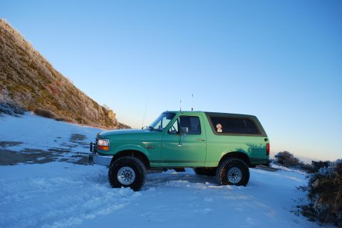 1996 Ford Bronco - A green 1996 Ford Bronco sits in the snow under a clear blue sky.