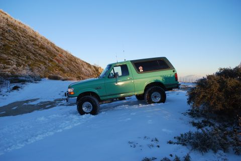 1996 Ford Bronco - A green 1996 Ford Bronco is seen in a snowy landscape under a clear blue sky.