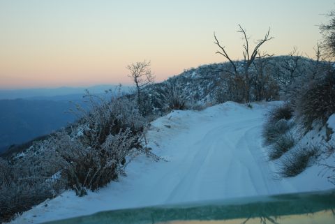 1996 Ford Bronco - A snowy mountain road winds through a winter landscape at dusk.