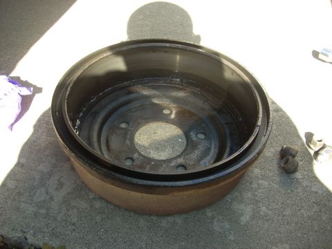 1989 Ford Bronco - A brake drum sits on a concrete surface next to lug nuts, with a shadow overhead.