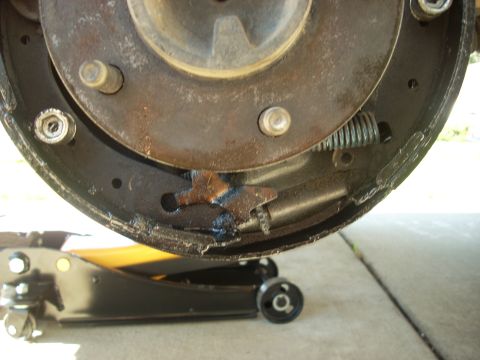 1989 Ford Bronco - Close-up view of a worn brake drum and shoes, with a hydraulic jack visible below.