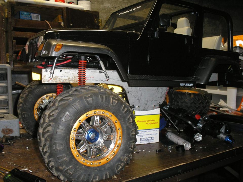 Black Jeep Wrangler with oversized tires and gold rims, appears to be undergoing modifications in a workshop