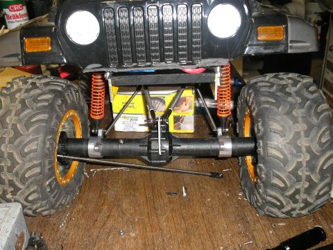 1994 Ford Escort - Close-up of an RC car's front suspension and drivetrain components, with large off-road tires.
