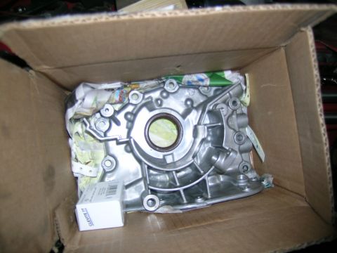 1995 Ford Probe - A new oil pump part is shown inside a cardboard box, partially wrapped in paper.
