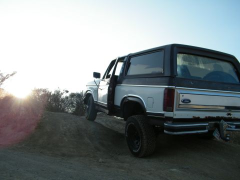 1982 Ford Bronco - A white and black Ford Bronco is parked on a dirt incline under a clear sky.