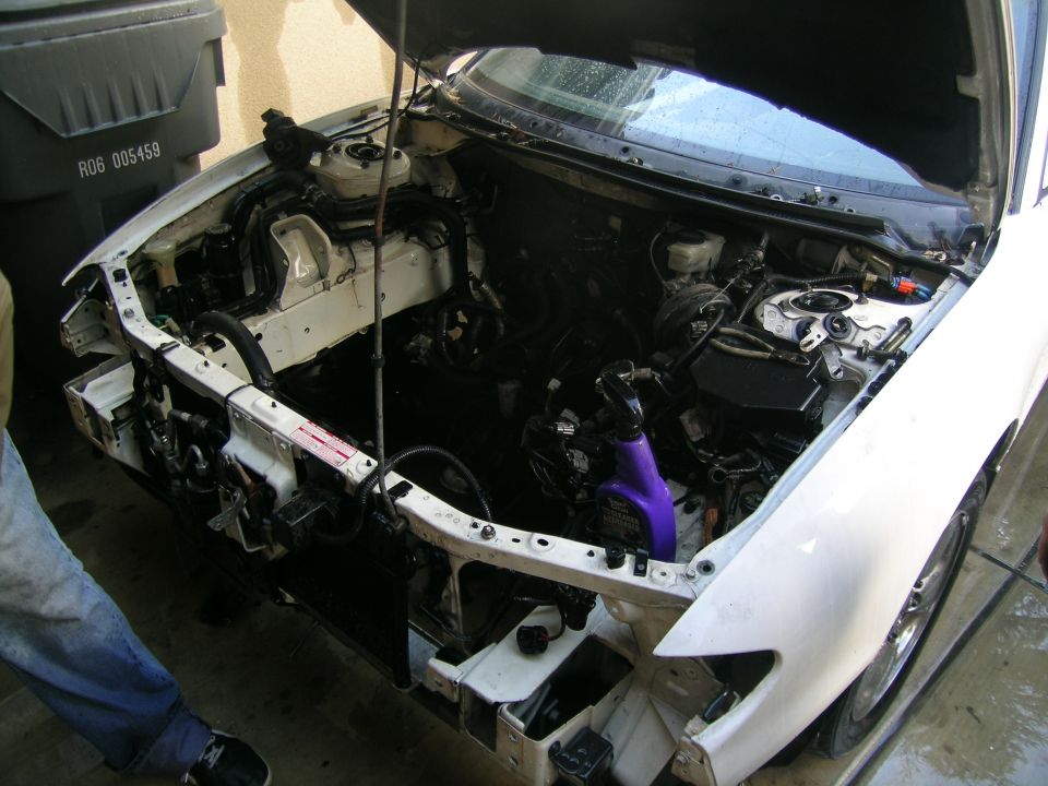 car engine bay, front bumper and grille removed, showing engine components and wiring