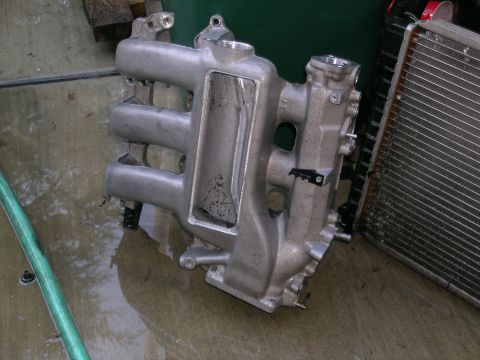 1993 Ford Probe - An aluminum intake manifold sits on a wet concrete surface beside a radiator.