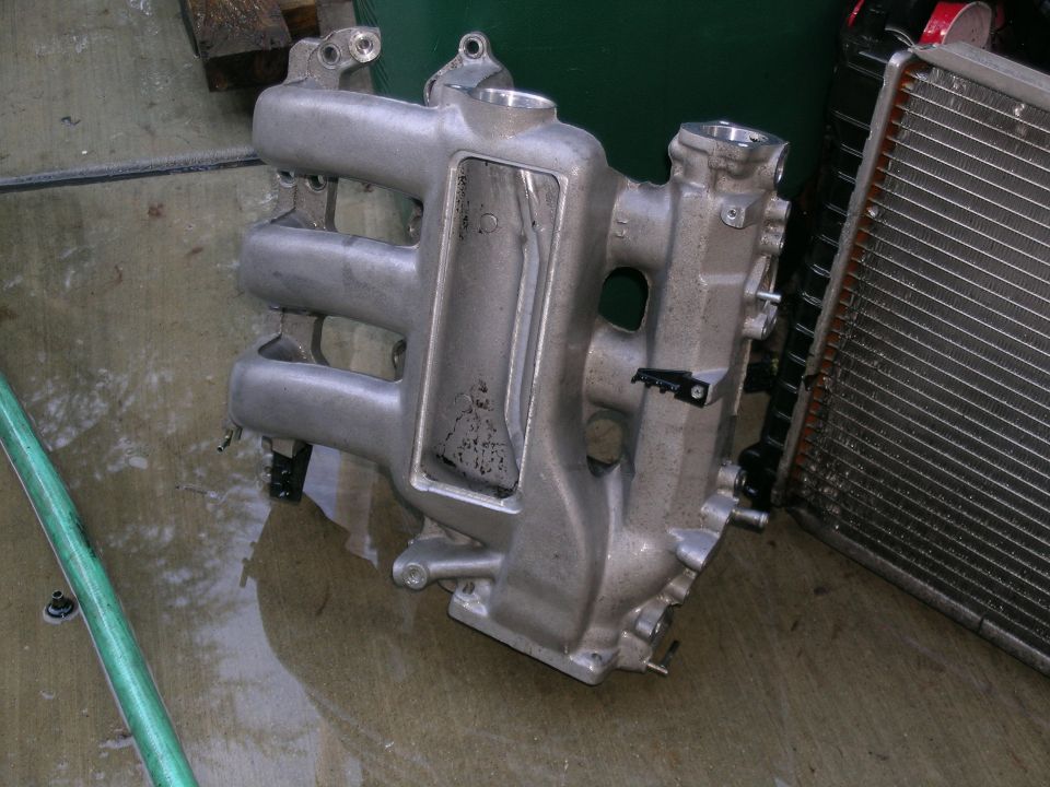 Aluminum intake manifold on wet concrete floor next to a radiator