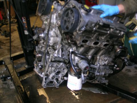 1993 Ford Probe - Engine assembly on a stand, being worked on by someone wearing blue gloves.