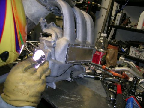 1993 Ford Probe - A person in a welding mask and gloves works on an intake manifold with various tools and supplies in the background.