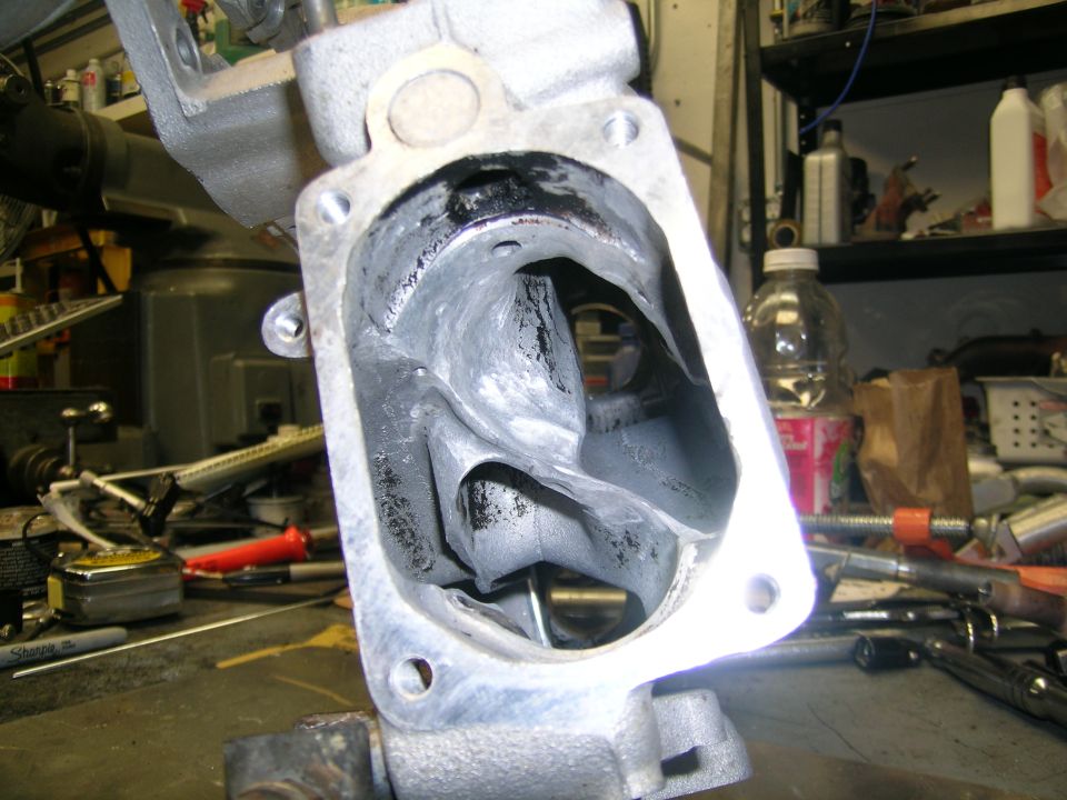 Turbocharger housing with internal vanes, covered in black residue, on a workbench with tools