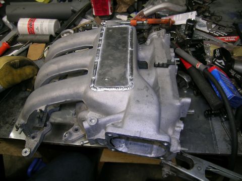 1993 Ford Probe - An intake manifold with visible welding repairs sits on a workbench surrounded by tools and parts.