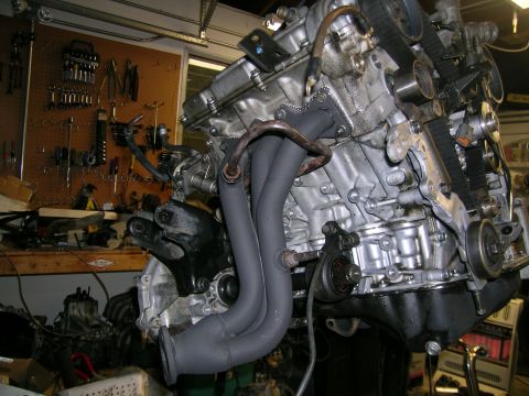 1993 Ford Probe - Engine assembly with visible timing belts and exhaust manifold in a cluttered garage setting.