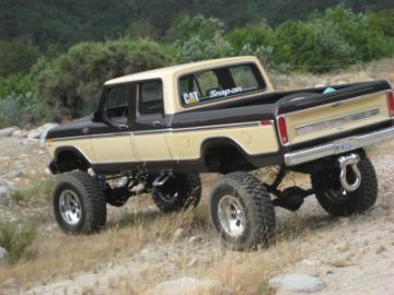 1982 Ford Bronco - A lifted two-tone pickup truck is parked on a dirt road with trees in the background.