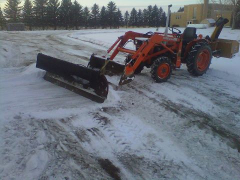 1994 Ford F-150 - An orange tractor equipped with a front plow and a rear-mounted snow blower sits on a snow-covered surface.