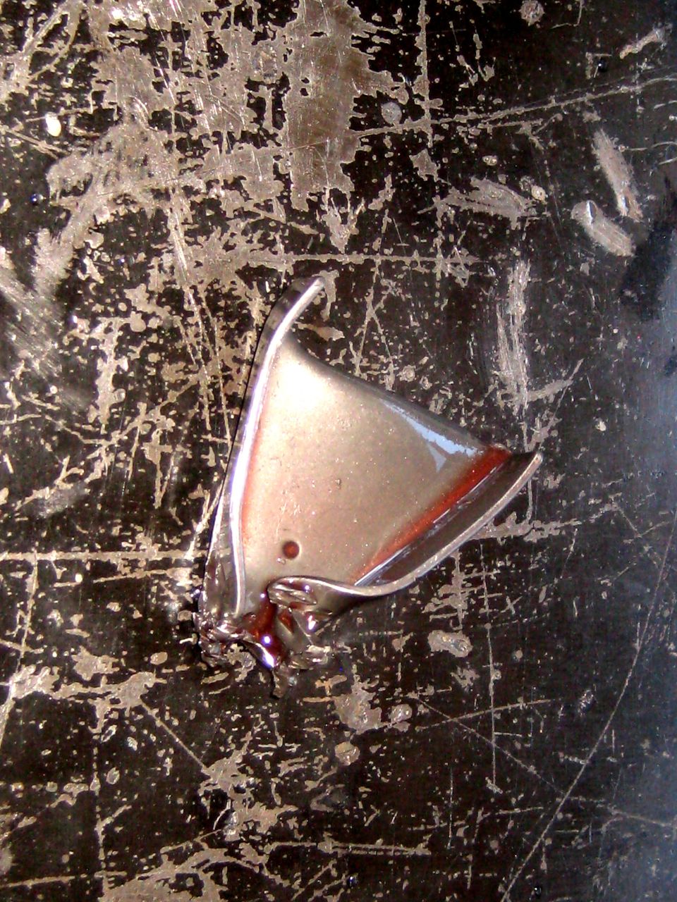 Chrome trim piece with red accent on scratched black surface