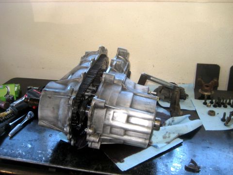 1996 Ford Bronco - Transfer case assembly with chain and gears, on a workbench with tools and parts nearby.
