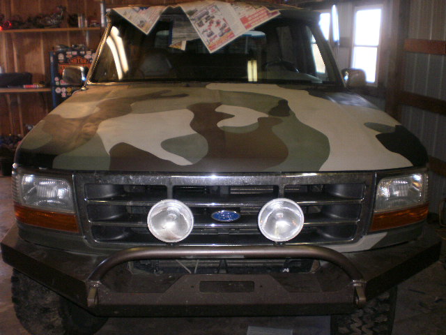 Front view of a Ford Bronco with camo hood and round driving lights in the grille