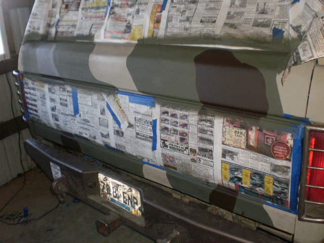 Truck tailgate masked with newspaper while camouflage paint is sprayed in a garage