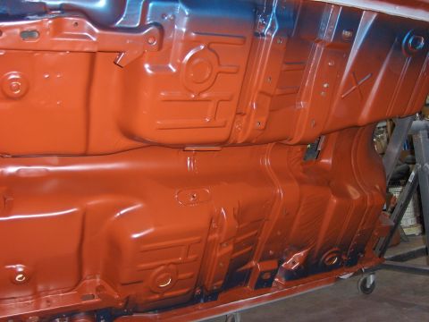 1972 Chevrolet Camaro - Car undercarriage coated in orange rust-proofing, showing structural details and some blue overspray.