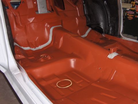 1972 Chevrolet Camaro - The interior floor pan of a car, coated in orange primer and sealed with grey seam sealer.