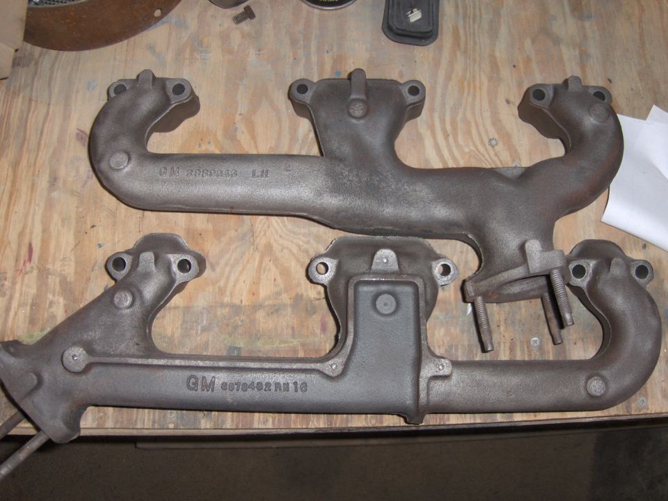 Two cast iron exhaust manifolds with GM part numbers visible