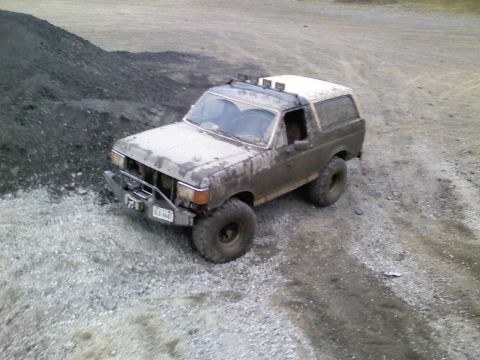 1990 Ford Bronco - 1990 Ford Bronco navigating rough terrain with mud caked on its body.