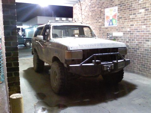 1990 Ford Bronco - This lifted Ford Bronco is parked under a covered area, possibly a car wash, with another vehicle visible in the background.