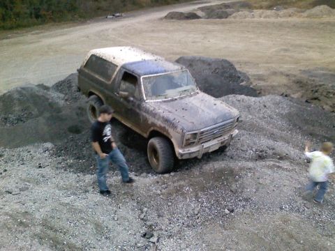 1990 Ford Bronco - A muddy Ford Bronco navigates a rough terrain of gravel and dirt piles.