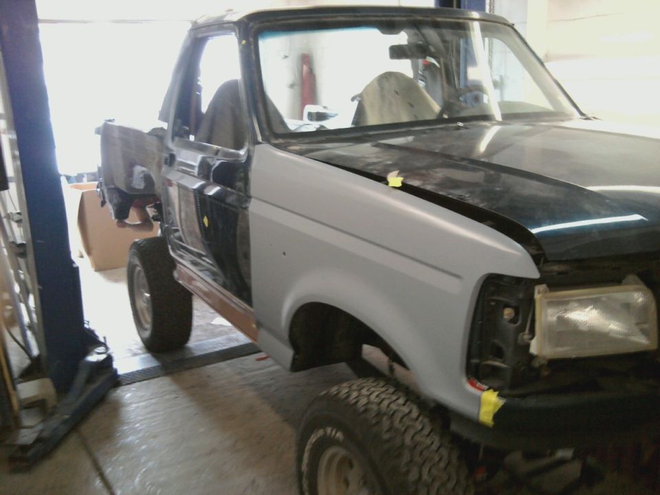 Primer-covered fender and black hood on unfinished truck, 3q-front view
