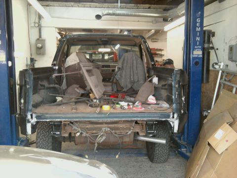 1994 Ford Bronco - Interior of a dark SUV, stripped down for repair, with parts and tools visible in the cargo area.