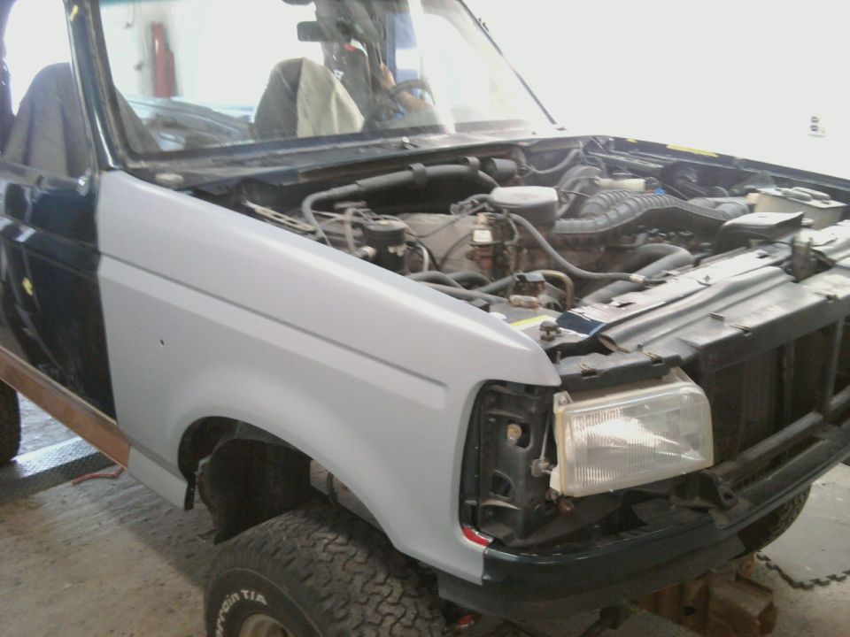Front fender is primer gray on a dark blue Ford Bronco with the hood open showing the engine