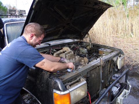 1985 Ford Bronco - A man works on the muddy engine of a truck, which appears to be from the early 1980s.