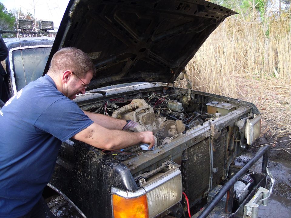 Mud-covered truck engine compartment with man working on it. Hood is open