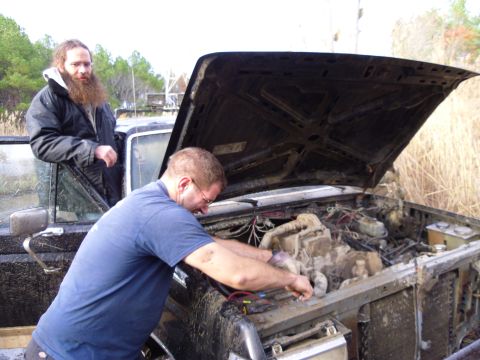 1985 Ford Bronco - Two men attend to the engine of a muddy 1985 Ford Bronco.