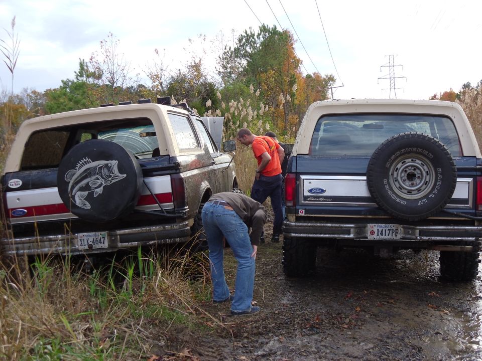 Two 1985 Ford Broncos stuck in mud, one with a bass fish spare tire cover