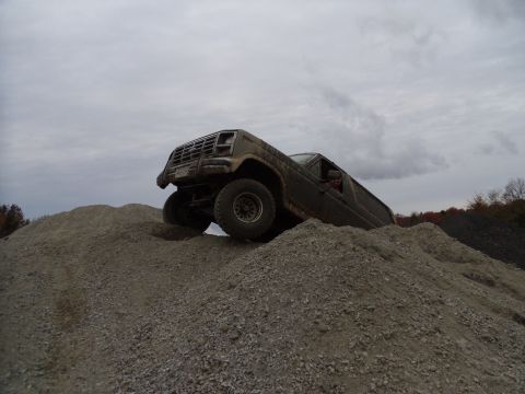 1985 Ford Bronco - This off-road vehicle is navigating a steep gravel incline under a cloudy sky.