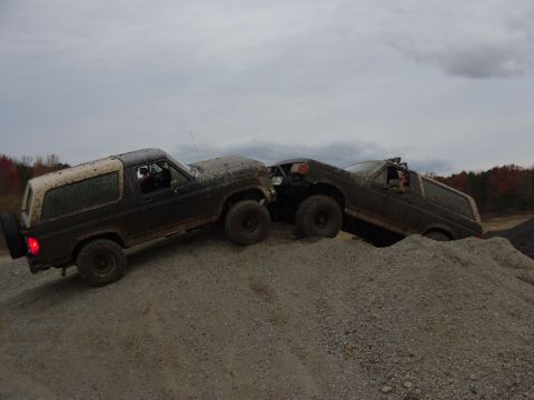 1985 Ford Bronco - Two 1985 Ford Broncos navigate a challenging off-road course, climbing a steep gravel incline under an overcast sky.