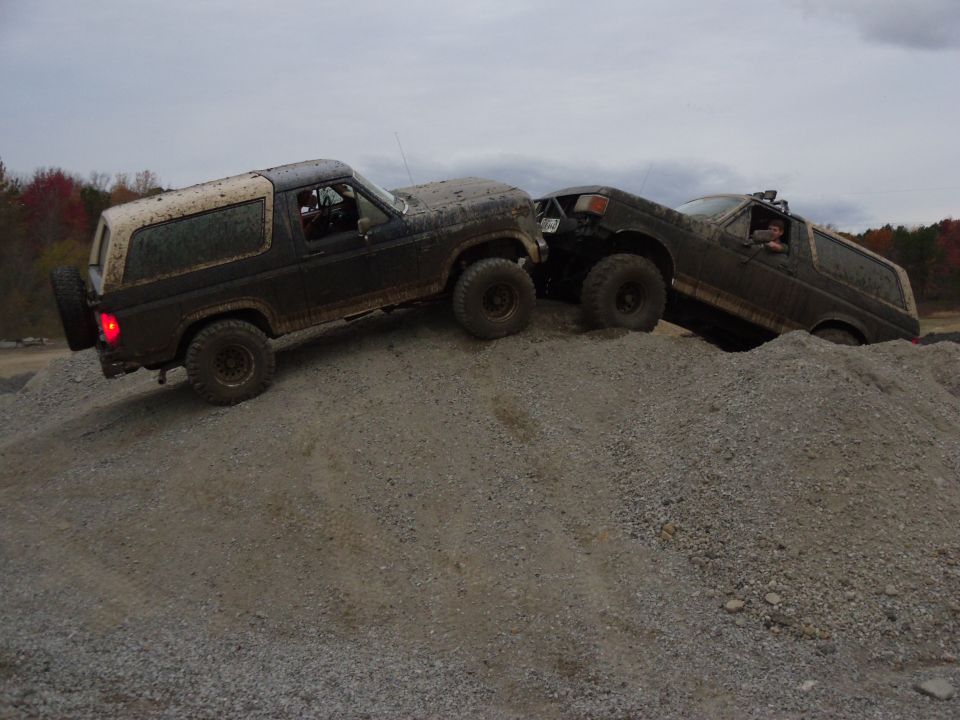 Two 1985 Ford Broncos climbing a steep gravel hill, one behind the other