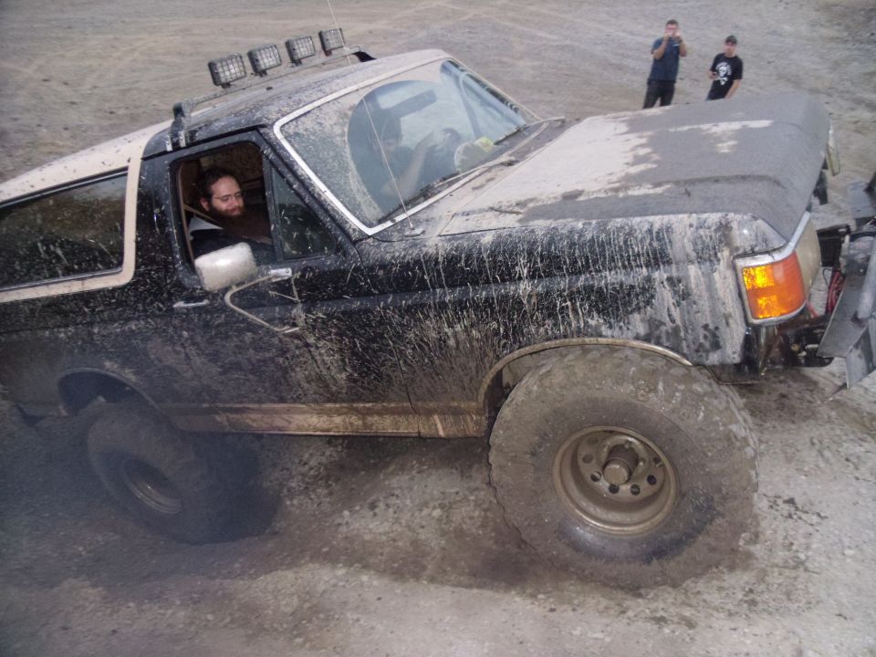 Mud-covered black Ford Bronco with a white top, seen from the front-right