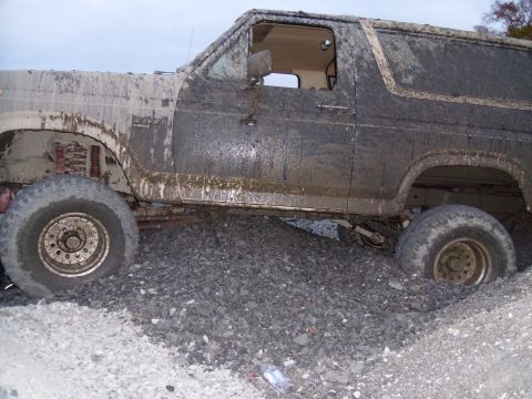 1985 Ford Bronco - This heavily soiled SUV appears to be stuck in a pile of gravel, with mud covering most of its exterior.