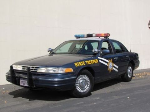 1991 Ford LTD Crown Victoria - A 1991 Ford Crown Victoria police car is parked in front of a wall, showing its full side profile and front.