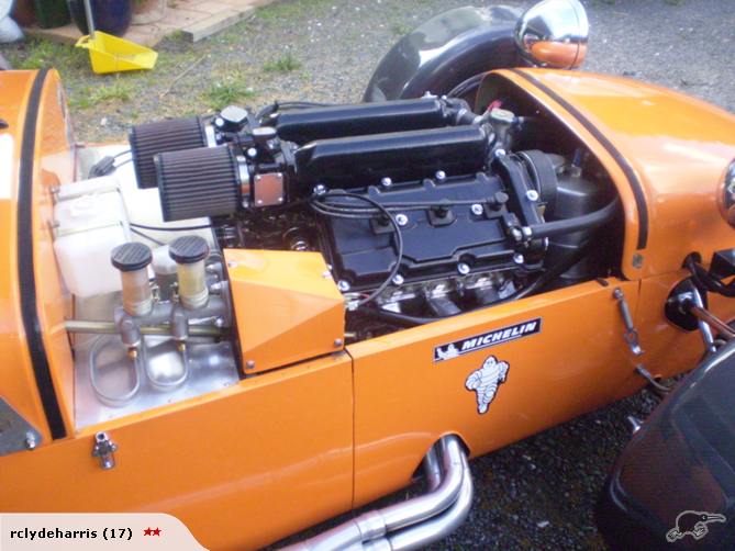 Orange sports car engine bay with dual carburetors and Michelin sticker
