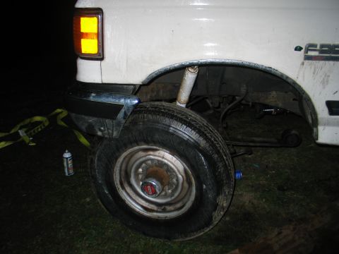 1984 Ford Bronco - Close-up of a white Ford truck's front wheel well and fender, with a yellow strap and spray can nearby.