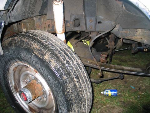 1984 Ford Bronco - Close-up view of the front wheel and suspension system of a vehicle, with a can of WD-40 visible on the grass below.